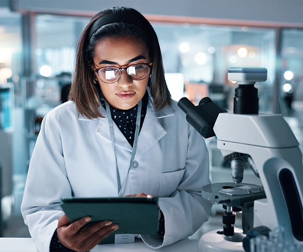 Female scientist with microscope holding tablet